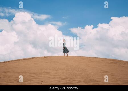 Schöne Landschaft in Sanddünen. Ein Mädchen in einem rosa, hellen Kleid geht durch die Wüste gegen den blauen Himmel. Safari in Kasachstan. Goldstrand von M Stockfoto