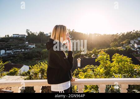 Blonde Frau raucht eine Zigarette auf einem Pavillon gegen Sonnenuntergang Stockfoto