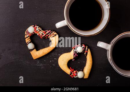 Studioaufnahme von herzförmigen Keksen und zwei Tassen Kaffee, die vor braunem Hintergrund stehen Stockfoto