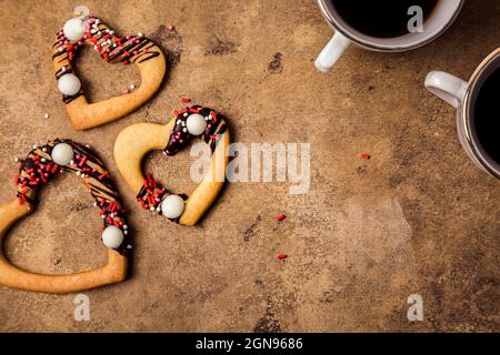 Studioaufnahme von herzförmigen Keksen und zwei Tassen Kaffee vor rotem Hintergrund Stockfoto