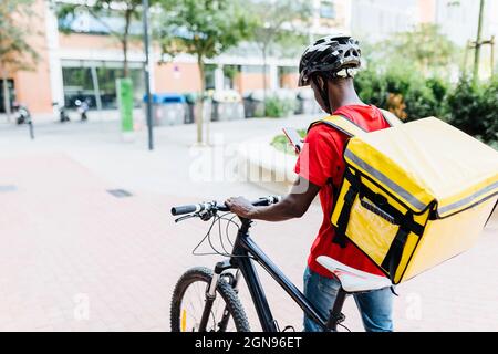 Der Lieferer benutzte ein Smartphone, während er auf dem Fußweg mit dem Fahrrad unterwegs war Stockfoto