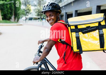 Glücklicher junger Mann mit Rucksack auf dem Fahrrad sitzend Stockfoto