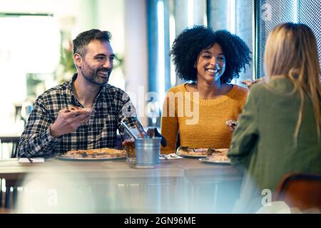 Glückliche männliche und weibliche Freunde genießen Pizza im Restaurant Stockfoto