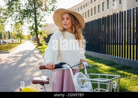 Junge blonde Frau mit Hut und Fahrrad im Park Stockfoto