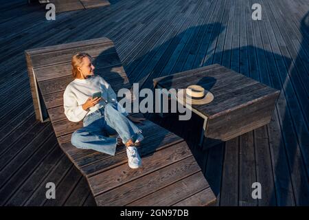 Frau mit Smartphone sitzt auf einer Holzbank Stockfoto