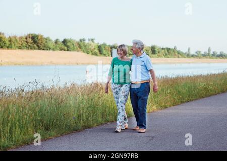 Lächelndes Seniorenpaar, das mit dem Arm auf der Straße herumläuft Stockfoto