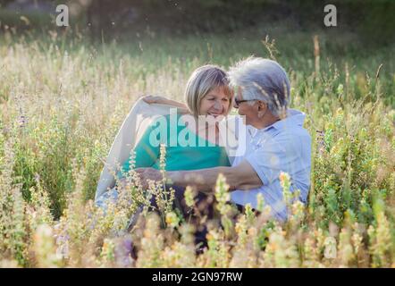 Mann, der die Frau mit einer Decke bedeckt, während er auf der Wiese sitzt Stockfoto