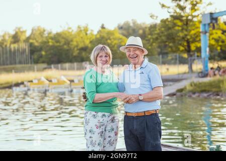 Fröhliches Paar, das die Hände hält, während es am See steht Stockfoto
