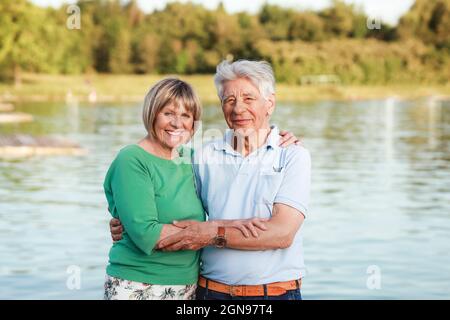 Lächelndes Seniorenpaar, das mit dem Arm am See herumsteht Stockfoto