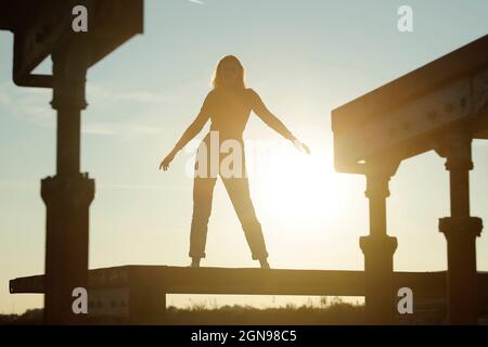 Silhouette Frau stehend mit ausgestreckten Armen während des Sonnenuntergangs Stockfoto