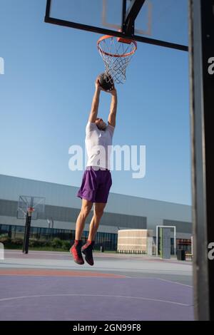 Männlicher Athlet springt und wirft den Ball in den Reifen während des Streetball-Trainings Stockfoto