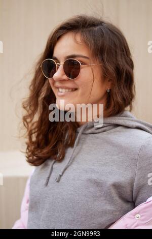 Eine junge Frau mit Sonnenbrille und Hoodie schaut zur Seite und lächelt. Stockfoto