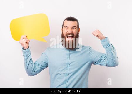 Aufgeregt bärtigen Mann macht die Gewinner Geste und hält eine Sprechblase über weißem Hintergrund. Stockfoto