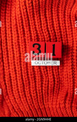 Holzwürfelkalender zeigt am 31. Oktober Halloween isoliert auf rotem Hintergrund rot gestrickter Pullover Stockfoto