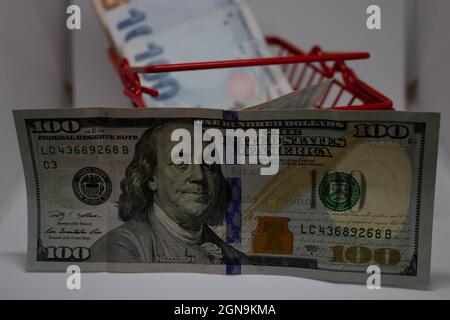 100-Dollar-Schein vor türkischen Lira in einem roten Warenkorb. Zeigt, wie wertvoll der Dollar gegenüber der Lira ist. Die türkische Lira ist sehr niedrig auf Kauf po Stockfoto