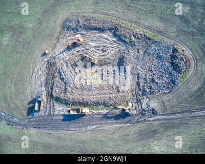 Baustellen-Luftaufnahme mit schweren Geräten, Erdbewegern, Muldenkipper, die an Bodenaushub in einem grünen Feld arbeiten, Victoria, Australien. Stockfoto