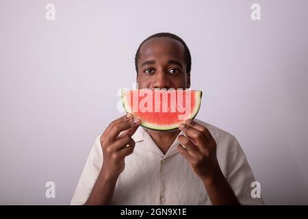 Lächelnder Mann mit einer Scheibe Wassermelone vor seinem Mund als Zeichen des Lächelns. Konzept für ein gesundes Leben und gesunde Ernährung Stockfoto