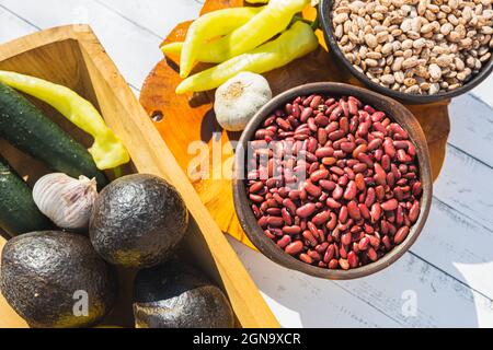 Bohnen in dunklen Schalen auf Holzhintergrund. Avocados, Knoblauch und grüne Chilischoten. Stockfoto