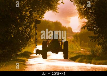 Landwirtschaftliche Arbeit, fährt man einen Traktor Pflug auf der Straße vor dem Hintergrund des Sonnenuntergangs Himmel , im Herbst Stockfoto