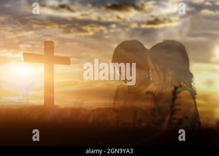 Zwei Schwestern, die Hände halten, beten Gott an und Preisen ihn im Hintergrund des Sonnenuntergangs. Christliches Religionskonzept. Stockfoto