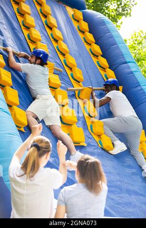 Männer klettern auf aufblasbare Rutsche Stockfoto