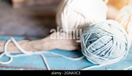 Kugeln aus weißem und beigem Garn auf hellblauem Holztisch. Fäden aus hochwertiger Wolle für Macrame und Kunsthandwerk. Stockfoto