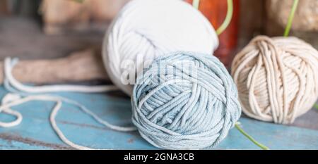 Kugeln aus weißem und beigem Garn auf hellblauem Holztisch. Fäden aus hochwertiger Wolle für Macrame und Kunsthandwerk. Stockfoto