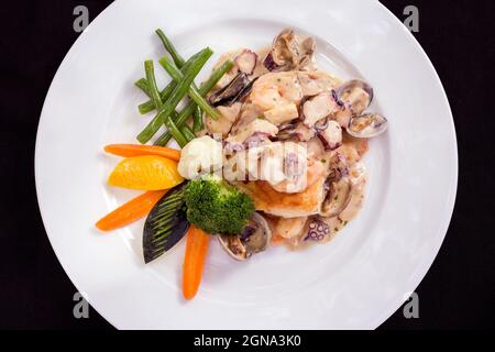 Nahaufnahme von Fisch in Meeresfrüchtegerauce mit Gemüse Krake Tintenfisch Muschel Garnelen gebadet Stockfoto