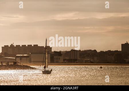 Silhouette eines Segelbootes auf dem Wasser mit dem Ufer im Hintergrund, goldene Stunde Stockfoto