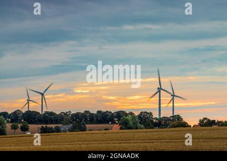 Aufnahme von Windturbinen in Bewegung in der Nähe von landwirtschaftlichem Ackerland während des Sonnenaufgangs Stockfoto