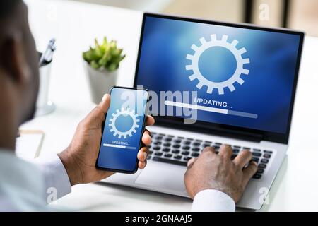 Afroamerikanischer Mann Tut Software-Update Auf Handy Und Laptop Stockfoto