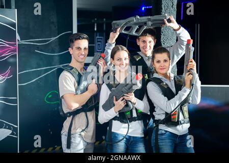 Vier Glückliche junge Männer eine Frauen mit Laser Pistolen in der Hand in dunklen Laser tag Zimmer posing Stockfoto