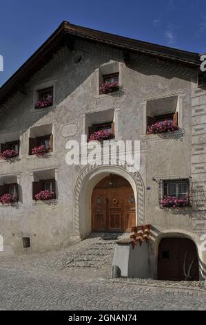 Schuppige Meerestiere und eine Meerjungfrau, in naiver oder primitiver Sgraffito verkratzt, schwimmen zwischen den Fenstern im ersten und zweiten Stock an der restaurierten Fassade dieses traditionellen Hauses in Scuol Sot, der Altstadt von Scuol in Graubünden oder Kanton Graubünden, Schweiz. Die Sgraffito-Dekoration unterstreicht auch die Fenster und den Eingang und die Fassade trägt eine Inschrift in Rätoromanisch, einer Vermächtnis-Sprache des römischen Reiches, die noch von vielen Menschen in Scuol gesprochen wird. Es enthält das Datum 1959, das Jahr, in dem das Anwesen renoviert wurde. Stockfoto