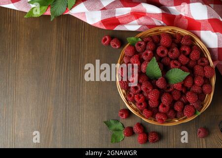 Himbeeren in einer Weidenschale und ein Geschirrtuch auf einem Holztisch. Stockfoto