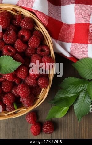 Himbeeren in einer Weidenschale und ein Geschirrtuch auf einem Holztisch. Stockfoto