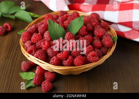 Himbeeren in einer Weidenschale und ein Geschirrtuch auf einem Holztisch. Stockfoto