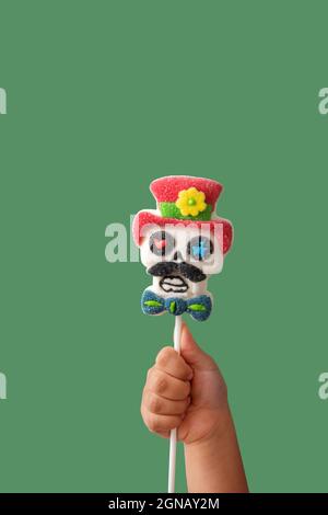 Kind Hand hält Süßigkeiten Schädel Lollipop auf grünem Hintergrund Stockfoto