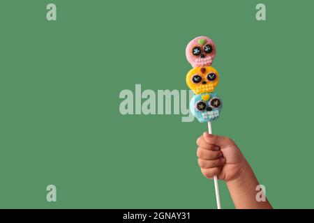 Kind Hand hält Süßigkeiten Schädel Lollipop auf grünem Hintergrund Stockfoto