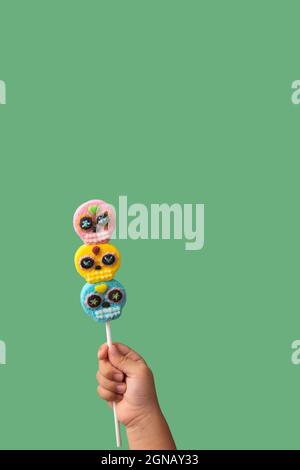 Kind Hand hält Süßigkeiten Schädel Lollipop auf grünem Hintergrund Stockfoto