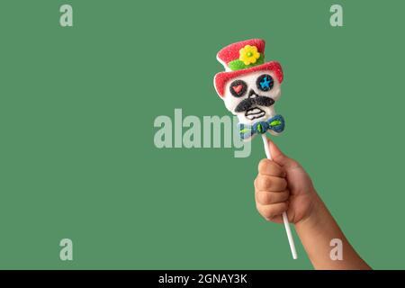Kind Hand hält Süßigkeiten Schädel Lollipop auf grünem Hintergrund Stockfoto