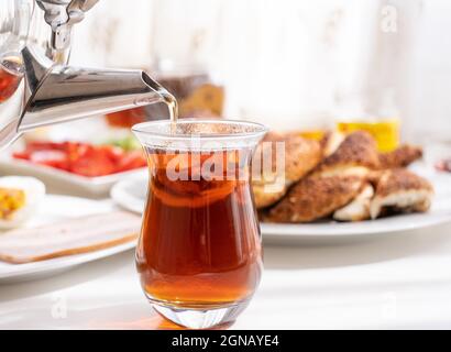 Gießt frischen türkischen Tee in ein Glas, Frühstückstisch im Hintergrund. Stockfoto