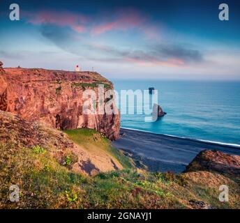 Dramatischer Sonnenuntergang im Dyrholaey Nature Reserve. Leuchtturm von oben vom Dyrholaey Bogen, Südküste Islands, Atlantik, Europa. Künstlerisch Stockfoto