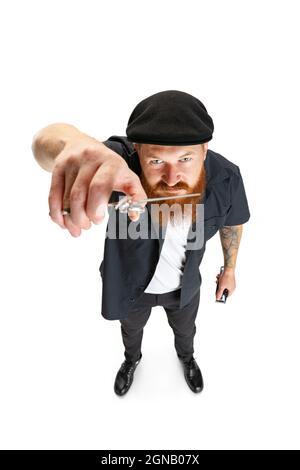 High-Angle-Ansicht von rotbärtigen Mann, Friseur oder Haarschneider in schwarzer Kappe isoliert auf weißem Studiohintergrund. Hält seine Arbeitsausrüstung. Stockfoto