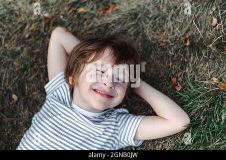 Kind liegt auf dem Rücken im Gras im Park. Junge chillen auf grünem Rasen. Kind entspannt sich draußen und ruht seinen Kopf auf der Gartenwiese Stockfoto