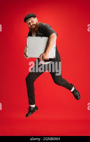 In voller Länge Porträt eines stilvollen rotbärtigen Mannes, Barbiers oder Haarschneiders, der isoliert auf rotem Studiohintergrund springt. Stockfoto