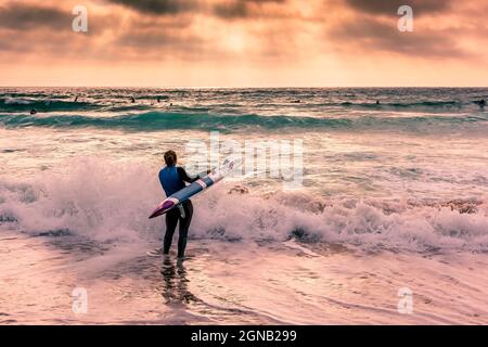 Am späten Abend wird ein Mitglied des Newquay Surf Lifesaving Club bei einer Trainingseinheit am Fistral Beach in Newquay in Cornwall beleuchtet. Stockfoto