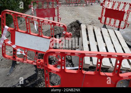 Notabschnitt der Straße mit einer Grube, eingezäunt mit roten Schutzbarrieren Stockfoto