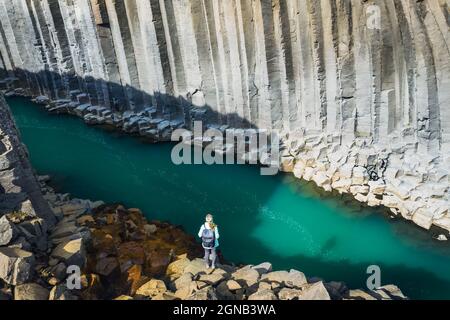 Wanderfrau mit Rucksack genießt den Studlagil Canyon. Einzigartige Jokulsa Basaltkolen und EIN Brufluss. Spektakuläre Outdoor-Szene von Island, Europa Stockfoto