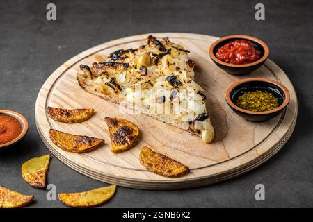 Argentinische Pizza mit Zwiebeln auf Schneidebrett mit verschiedenen Belägen und Bratkartoffeln im Ofen. Stockfoto