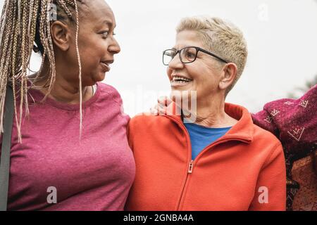 Glückliche ältere Frauen aus verschiedenen Ethnien lachen gemeinsam im Freien - Fokus auf das rechte weibliche Gesicht Stockfoto